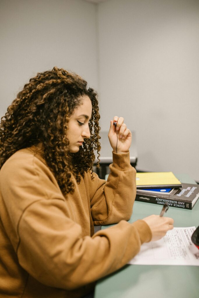A female student intently studying for an exam at a desk inside a classroom.