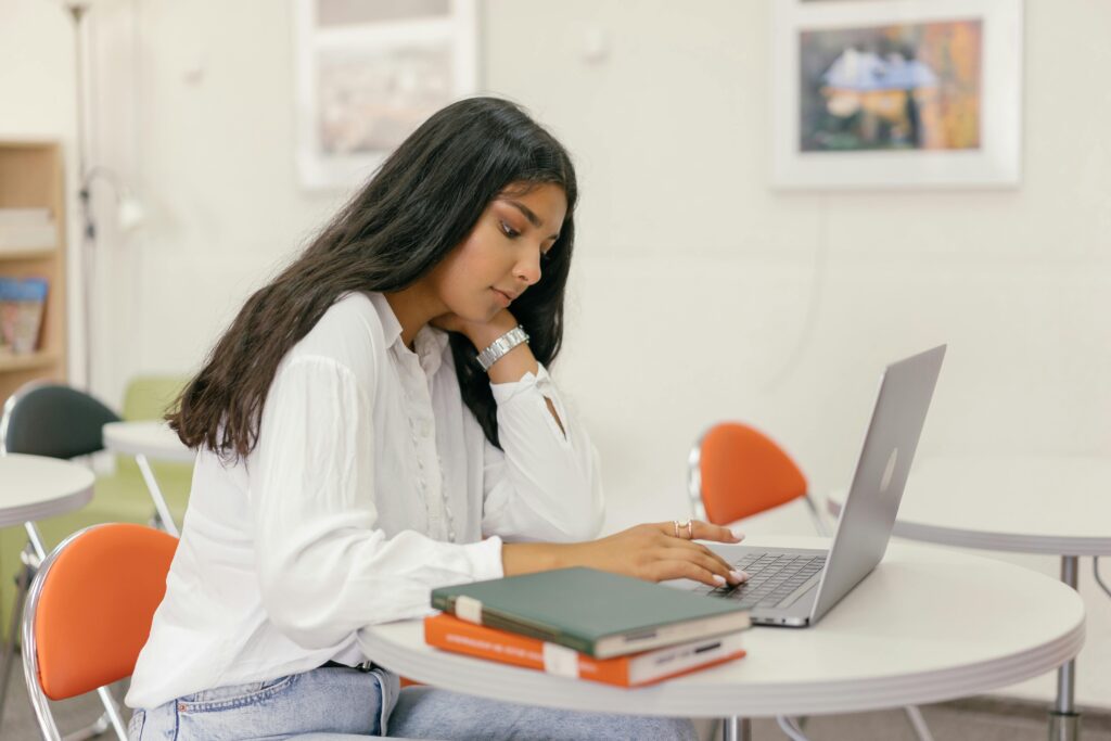 A young woman wearing white long sleeves studies with a laptop in a classroom setting.